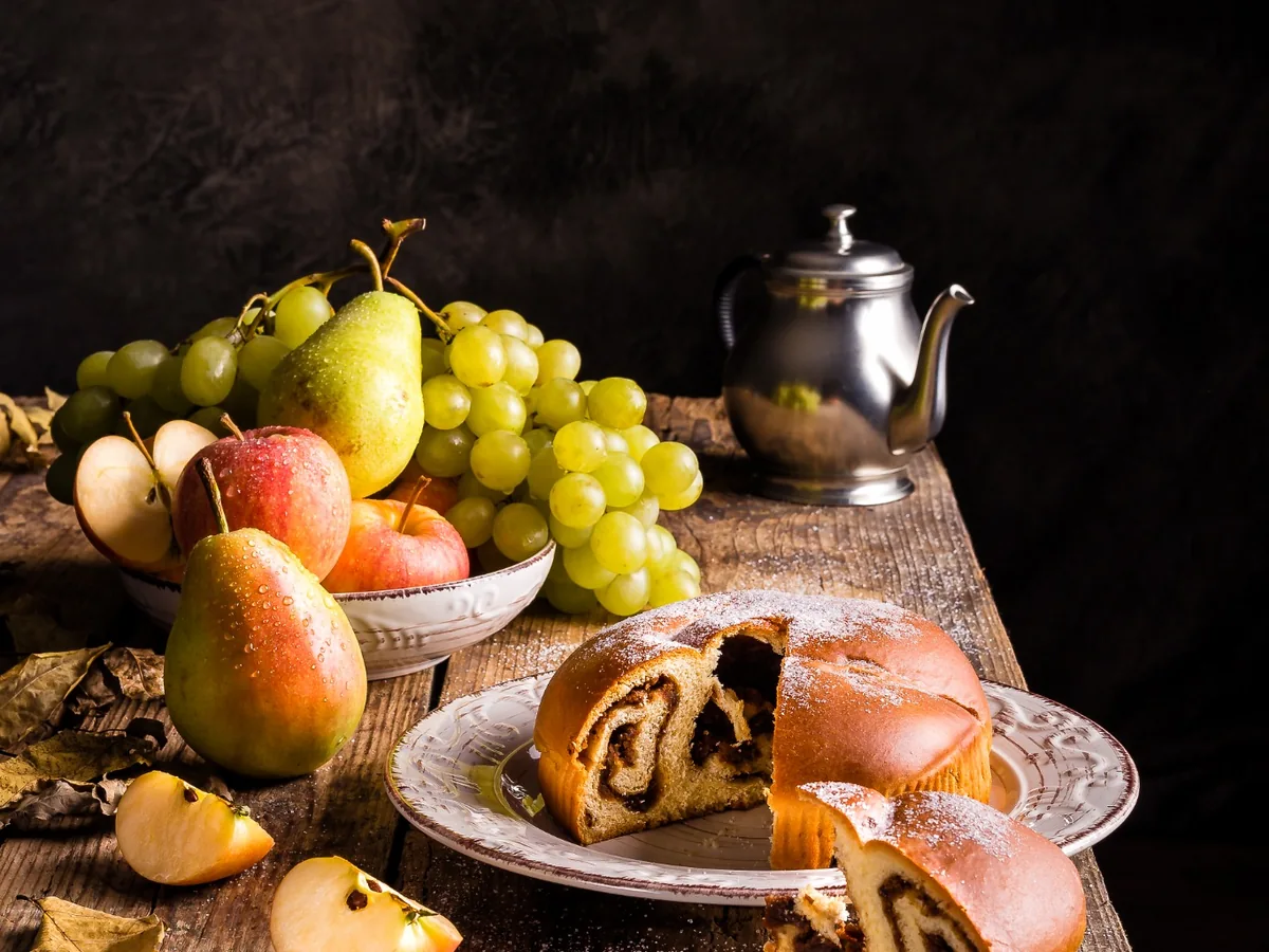 Fotografia still life di gubana, mele, pere e uva su tavolo rustico con luce direzionale