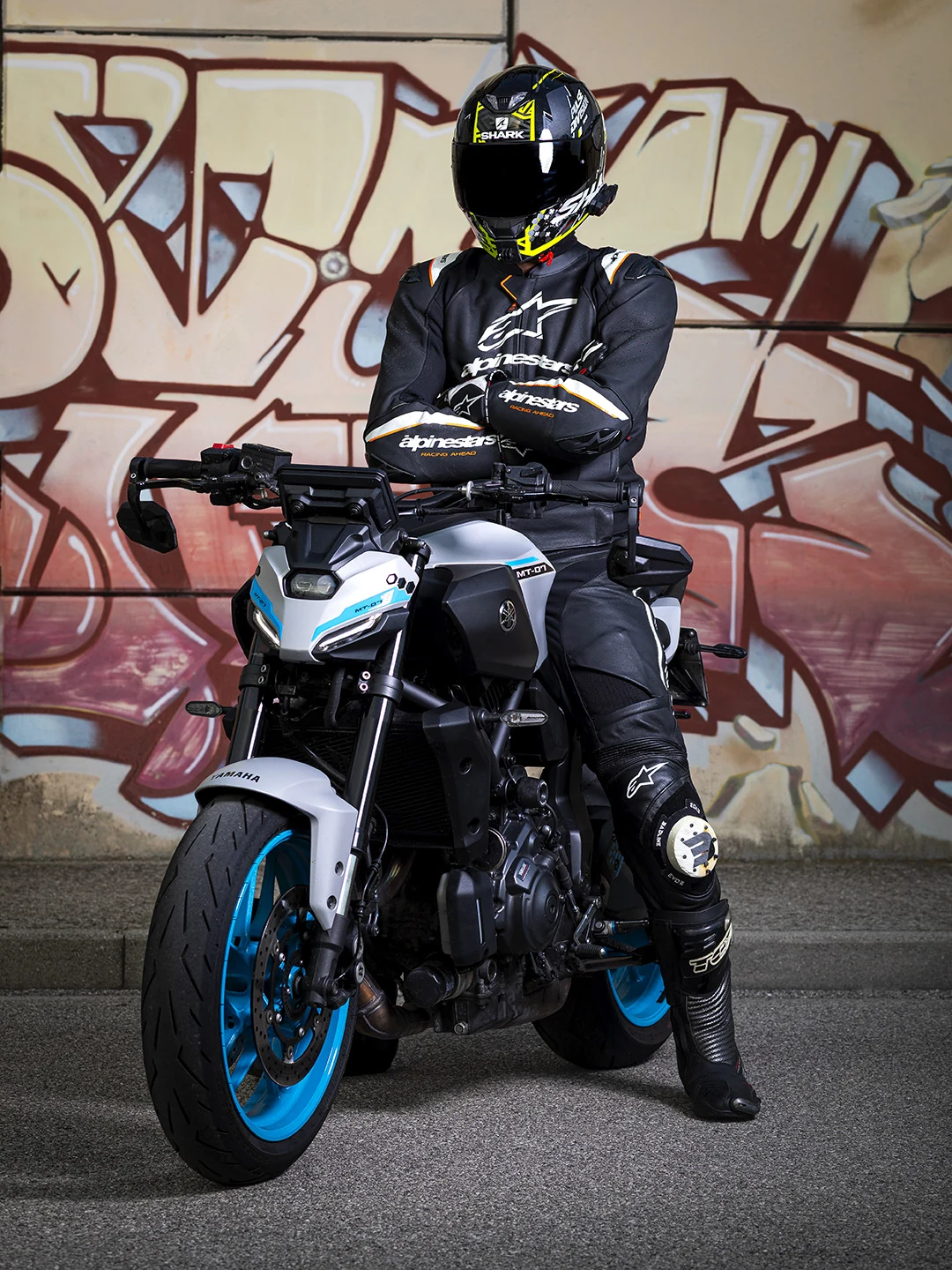 Motociclista con casco e tuta nera seduto sulla Yamaha MT-07 davanti a un muro con graffiti